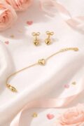 Gold heart earrings and bracelet on soft pink fabric with roses.