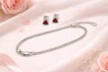Sterling silver necklace and earrings with red accents on soft pink fabric.