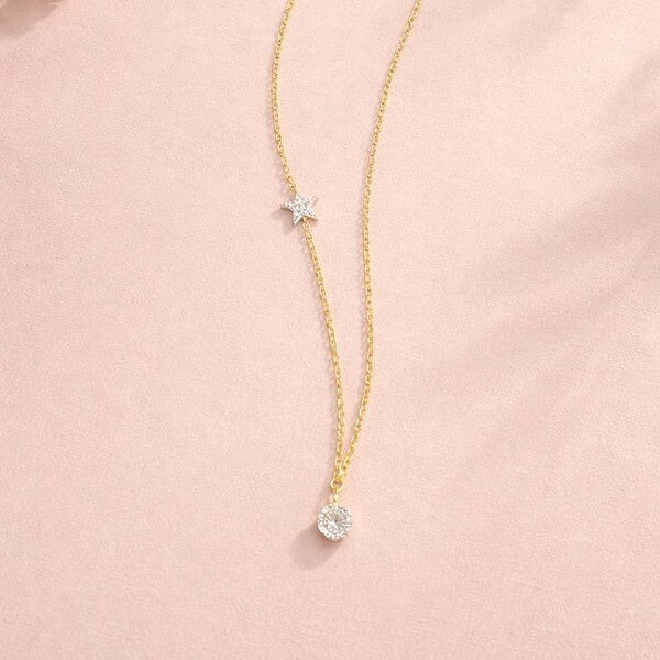 Gold necklace with a sparkling pendant on a pink background.