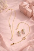 Gold-plated silver necklace and earrings with star designs on pink fabric.
