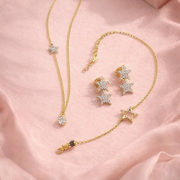 Gold-plated silver necklace and earrings with star designs on pink fabric.