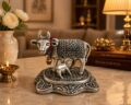 Silver-colored cow figurine with intricate patterns and a small calf at its feet.