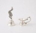 Silver peacock figurine and diya holder for temple decor.