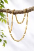 Gold chain necklace hanging on a tree branch with green leaves in background.