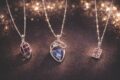 Three delicate silver necklaces with colorful gemstone pendants on a dark background.