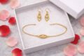 Gold silver jewelry set with earrings and bracelet in a white box.