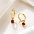 Gold hoop earrings with red gemstone charms on a white surface.