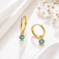 Gold hoop earrings with blue gemstone charms on white fabric background.