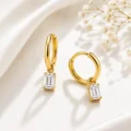 Gold hoop earrings with rectangular clear stones on a soft fabric background.