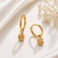 Gold hoop earrings with a dangling sparkling pendant on a satin background.