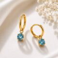 Gold hoop earrings with blue gemstones on a soft fabric background.