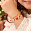 Gold charm bracelet with holiday-themed charms on a woman's wrist.